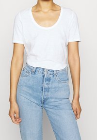 Weißes T-Shirt mit kurzen Ärmeln und rundem Ausschnitt, kombiniert mit hellblauen High-Waist-Jeans. Minimalistisches Design, weicher Stoff.