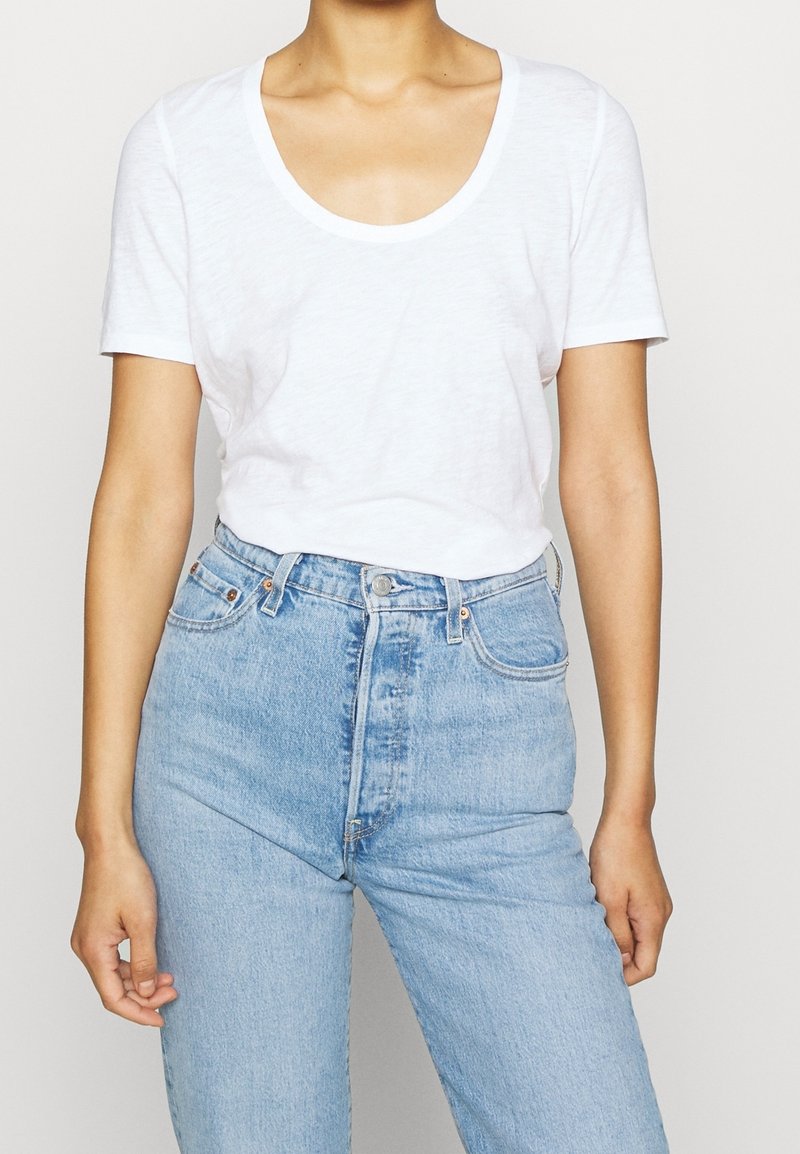 Weißes T-Shirt mit kurzen Ärmeln und rundem Ausschnitt, kombiniert mit hellblauen High-Waist-Jeans. Minimalistisches Design, weicher Stoff.