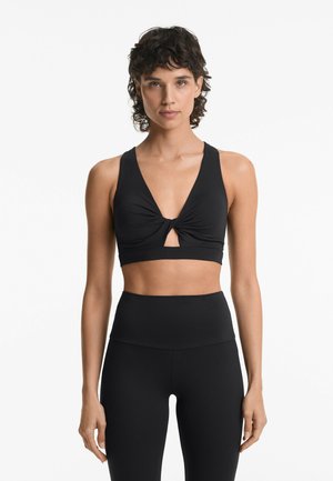 Zwarte sport-bh met een diepe V-hals, gedraaide voorkant en sleutelgatuitsnijding. Aansluitende stijl, zachte textuur, gecombineerd met zwarte high-waisted leggings.