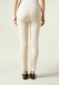 Leggings ajustés beiges avec une large ceinture élastique, une texture lisse et un design simple, associés à des chaussures plates noires.