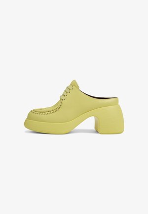 Yellow leather mules with a rounded toe, intricate stitching, and a thick, curved block heel. Smooth texture and minimalist design.