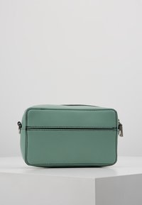 Borsa da toeletta rettangolare in pelle di un verde chiaro con cuciture nere, con una cerniera superiore e tirazip in argento, posizionata su una superficie bianca.