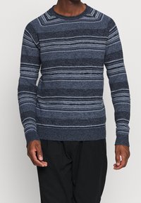 Námořnický modrý pletený svetr s horizontálními pruhy v různých odstínech modré a bílé, s kulatým výstřihem a žebrovanými manžetami a lemem.