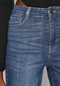 Τζιν σορτς σε μέτρια μπλε απόχρωση, με κλασικό σχέδιο πέντε τσέπες, ορατή ραφή και κουμπί κλεισίματος σε επίπεδη μέση.