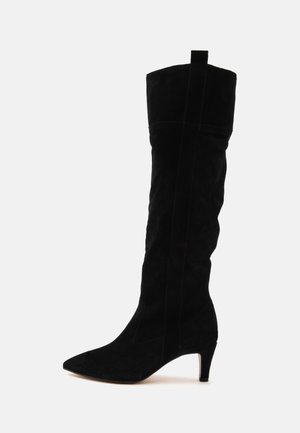 Schwarzer kniehoher Wildlederstiefel mit spitzer Spitze, mittelhohem Stilettoabsatz und Zuglasche, seitlich auf weißem Hintergrund dargestellt.