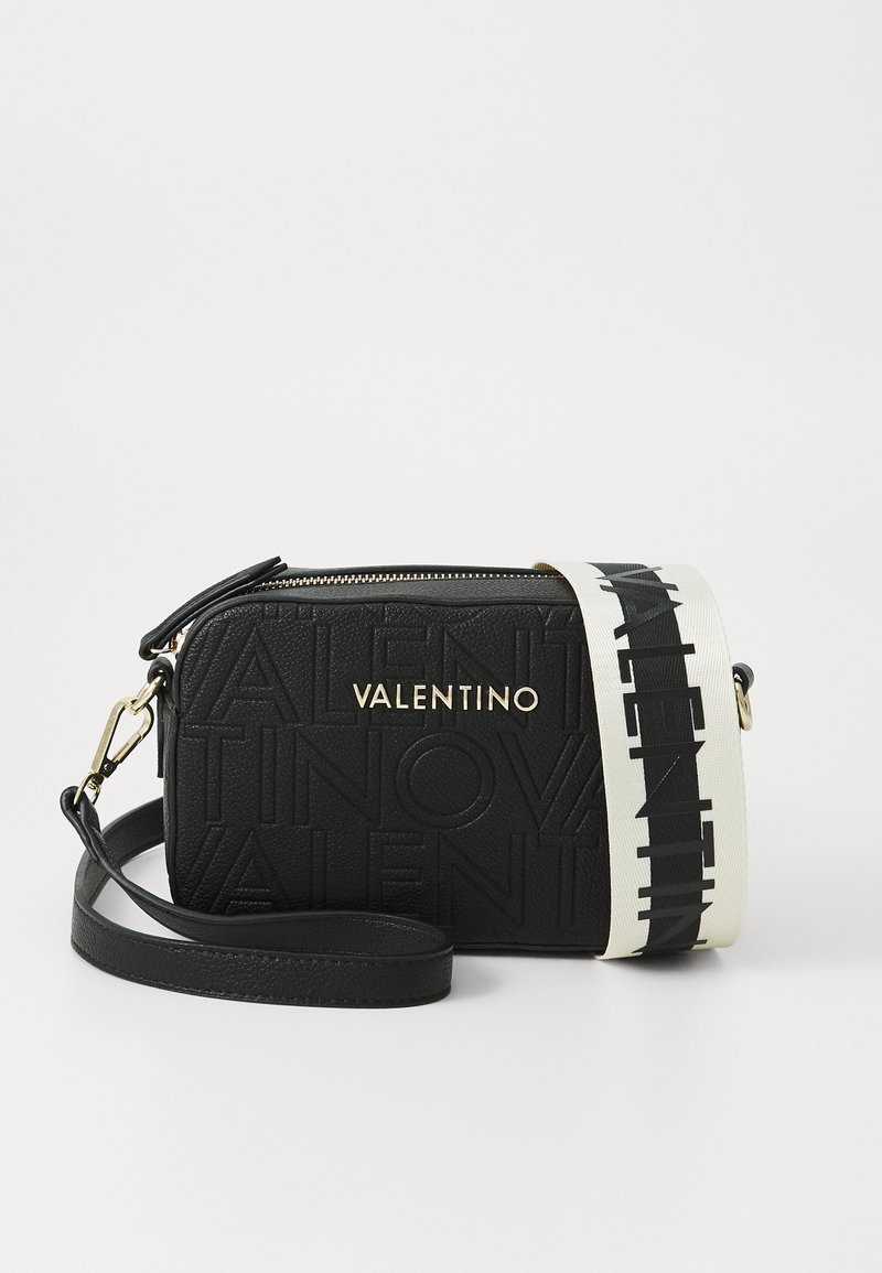 Črna usnjena torbica čez ramo z vgraviranim logotipom "VALENTINO", zlatim kovinskim okovjem in kontrastnim belim pasom, ki vsebuje ponovljen vzorec logotipa. Zapiranje na zadrgo.