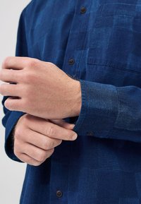 Camicia di flanella blu navy a quadri, con chiusura a bottoni e una tasca sul petto. Tessuto liscio e maniche lunghe.