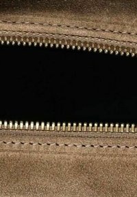 Dents de fermeture éclair en métal sur un tissu texturé beige avec des coutures détaillées des deux côtés et un tissu noir à l'intérieur de l'ouverture.