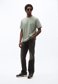 Svetlozelené bavlnené tričko vo voľnom strihu; tmavosivé rifle s vyblednutou textúrou; čierne a krémové športové topánky; čierne slnečné okuliare.