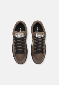 Hnedé kožené tenisky s čiernymi šnúrkami, s bielymi bočnými akcentmi a značkou Converse na jazyku a vnútorných vložkách. Zaoblený tvar špičky.