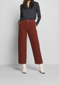 Marinebluse mit weißen Punkten; V-Ausschnitt. Braune Cordhose mit weitem Bein. Helle Ankle Boots. Einfarbiger, strukturierten Stoff.