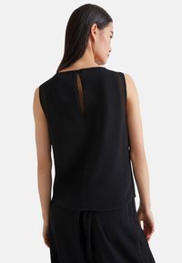 Top nero senza maniche con scollo rotondo, pannello posteriore trasparente e una leggera fessura sul retro. Tessuto morbido e vestibilità rilassata.