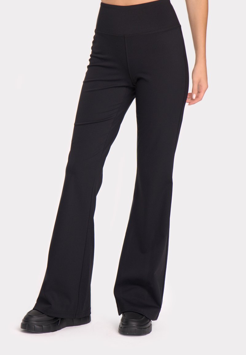 Črne, razširjene legice z visokim pasom, narejene iz elastične tkanine, z ravnimi šivi in gladko, mat teksturo.