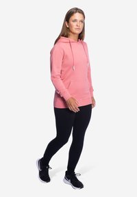 Rosa Kapuzenpullover mit verstellbaren Kordeln, Kängurutasche und gerippten Bündchen, kombiniert mit schwarzen Leggings und Sportschuhen. Einfaches Design.