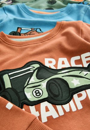 En stapel barntröjor med racerbilsdesign, där den orange tröjan har siffror och texten "RACE CHAMP".