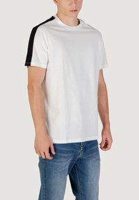 T-shirt bianco in cotone con accenti neri sulle spalle, collo a giro, maniche corte e vestibilità rilassata. Texture liscia e design classico.
