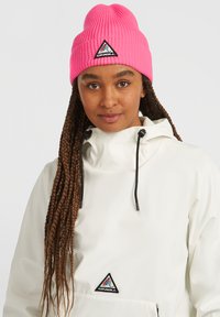 Bílý pulovrový kabát s vysokým límcem a černým stažením. Růžová pletená čepice s černou trojúhelníkovou nášivkou. Tmavé spletené vlasy viditelné.