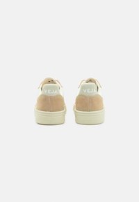 Beige mocka och vita lädersneakers med en texturerad yta, som har en framträdande "VEJA"-logotyp på baksidan och en ljusfärgad sula.
