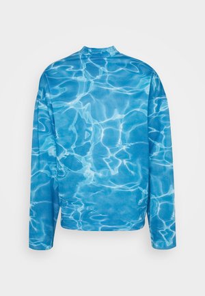 Camicia azzurra a maniche lunghe con colletto alto, caratterizzata da un motivo a onde d'acqua che ricorda la superficie di una piscina.