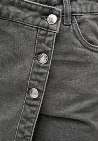 Κοντινό πλάνο σκούρων γκρι τζιν από denim που δείχνει τρία ασημένια κουμπιά και το άκρο της τσέπης με ορατή ραφή.