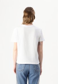 T-shirt bianco a maniche corte con scollo a giro, mostrato da dietro, abbinato a jeans a vita alta azzurri chiari con ricami floreali.