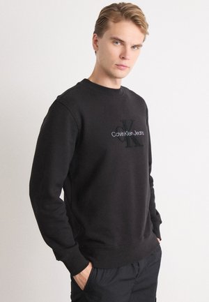 Felpa nera in morbido tessuto con scollo rotondo. Presenta il logo ricamato "Calvin Klein Jeans" nella parte anteriore. Polsini e orlo accentuati.