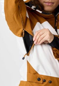 Orange and white waterproof jacket with an adjustable hood and zippered pockets. Features visible stitching and a buttoned closure at the waist.