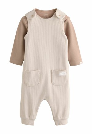 Cremefarvet ribbet jumpsuit med rund hals, to forlommer og trykknapper på skuldrene. Lange brune ærmer er vedhæftet til lag-på-lag brug.