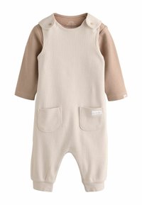 Combinaison côtelée crème avec un col rond, deux poches avant et des pressions aux épaules. Des manches longues marron sont attachées pour le superposition.