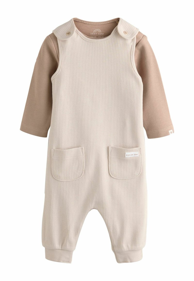 Combinaison côtelée crème avec un col rond, deux poches avant et des pressions aux épaules. Des manches longues marron sont attachées pour le superposition.