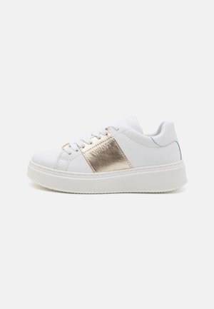 Baskets blanches avec une semelle surélevée, présentant une bande métallique dorée et un logo sur le côté. Texture lisse et fermeture à lacets.