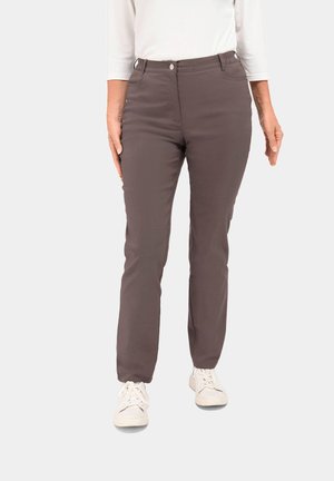 Bruine slim-fit broek met een gladde structuur. Voorzien van een knoop en ritssluiting aan de voorkant, schuine zakken en riemlussen. Draagt bij witte sneakers.