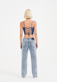 Top in denim corto con schiena lacciata, abbinato a jeans azzurri a vita alta con cinque tasche e un fit rilassato.