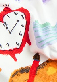 Bunt gemusterter Baumwollstoff mit einem roten Wecker, abstrakten Mustern in Grün und Lila sowie Illustrationen von orangefarbenen Kerzen.