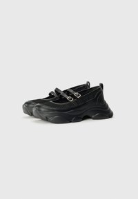 Scarpe slip-on nere con tomaia in rete e pelle, caratterizzate da due cinghie con fibbie e una suola spessa e arrotondata per un maggiore comfort.