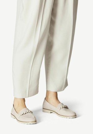 Beige slip-on sko med en flettet detalje, der har en tekstureret overdel og en lysefarvet gummisål. Sammen med cremegule, brede bukser.