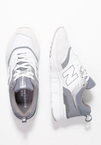 Ett par vita och grå New Balance 997H-sneakers, med en övervy av vänster sko och en sidovy av höger sko på en vit bakgrund.