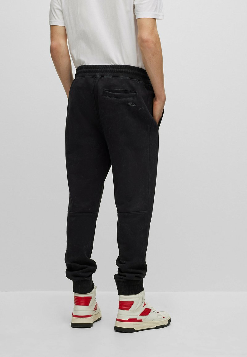 Pantaloni jogger neri con vita elastica, tasche laterali e tasca posteriore con il logo "BOSS". Abbinati a sneakers alte bianche e rosse.