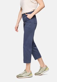 Persona vistiendo pantalones cortos azul marino, top sin mangas beige y zapatillas casuales verdes y beige caminando.