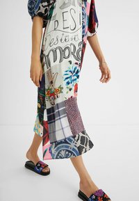 Multifarvet patchwork kjole med grafiske designs og broderede slides med sort bund og blomsterdetaljer, der fremhæver en tekstureret look.