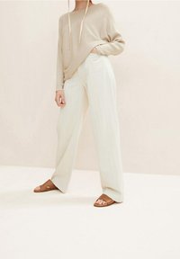 Beige geripptes Langarmshirt mit Bindungen, lockere weiße weite Hose und braune Slipper. Weicher Stoff und lässige Passform.