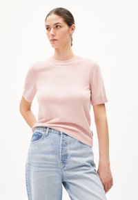 Light pink short-sleeve sweater with a crew neckline, smooth texture, and ribbed cuffs, paired with light blue denim jeans.