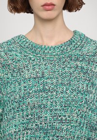 Strickpullover in Grüntönen und Grau mit einem breiten, gerippten Halsausschnitt. Verfügt über ein strukturiertes, gemustertes Gewebe über den gesamten Stoff.