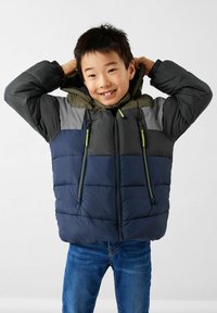 Veste matelassée avec un design coloré en bleu marine, gris et vert olive, dotée d'une fermeture éclair à l'avant et de deux poches latérales zippées.