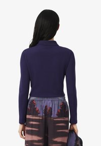 Marineblauwe polo met lange mouwen en een kraag. Het shirt heeft een aansluitende pasvorm, gecombineerd met losse, gestreepte multikleurige broek.