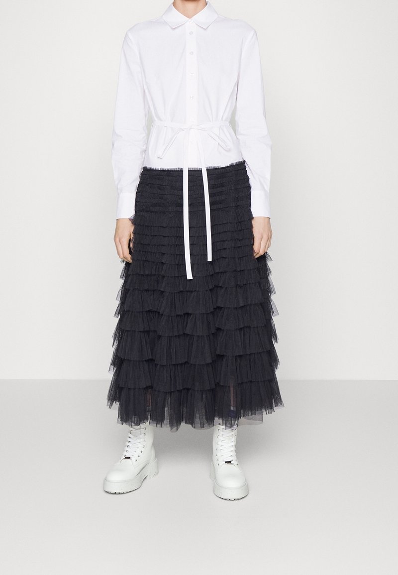 Camicia bianca con bottoni e maniche lunghe; abbinata a una gonna in tulle nera a strati; stivali alla caviglia bianchi con lacci; semplice fiocco in vita.