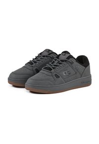 Zapatillas grises con una parte superior de cuero suave, detalles en negro, perforaciones, cordones trenzados y una suela de goma en un tono marrón contrastante.
