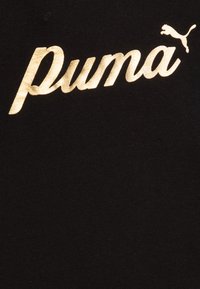 Camiseta de algodón negra con un prominente logo dorado de "Puma". Textura de tela suave con un diseño claro y audaz, y un pequeño acento del logo.