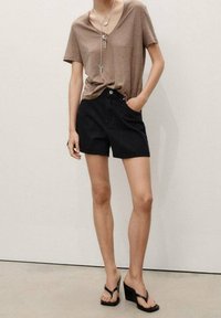 Camiseta marrón de pico, pantalones cortos de mezclilla negra de cintura alta y sandalias negras de cuña. Presenta collares de capas y un corte relajado.