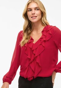 Blusa in chiffon rosso con scollatura a V, dettagli arricciati lungo la parte anteriore e lunghe maniche trasparenti con polsini elasticizzati.